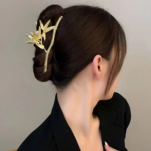 Close-up of golden bamboo leaf hair claw with pearl detail on a woman's bun hairstyle