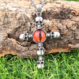 Gothic stainless steel skull cross necklace with a red evil eye stone on bark background