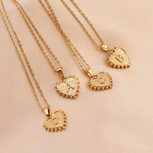 Detailed view of four gold heart initial necklaces on elegant pink silk fabric