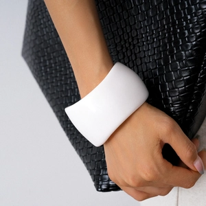 Detail of a white chunky resin geometric bangle on wrist with a textured black background