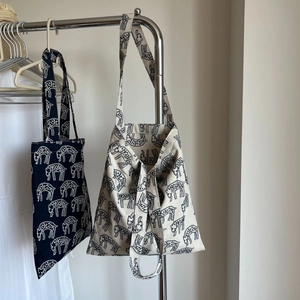Detail of navy and off-white canvas tote bags with animal prints hanging on a metal rack