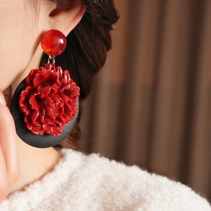 Détail de boucles d'oreilles fleur rouge avec base noire sur modèle en vue rapprochée