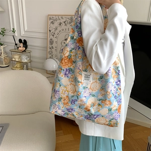 Dettaglio della borsa tote in tela floreale indossata da modella in abito bianco