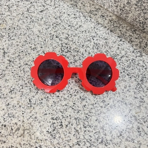 Detail shot of red flower-shaped kids' sunglasses with round lenses on a stone surface
