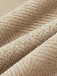 Macro shot of heavy beige knit fabric showing geometric diamond texture and soft drape