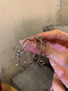 Close-up of large silver hoop earrings with 3D bow accents held in hand