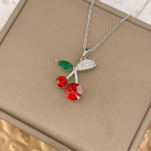 Detail of red cherry pendant with crystal leaves on a beige jewelry box