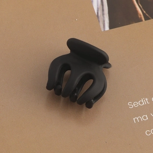 Macro detail of a mini matte black hair claw clip on a textured magazine page