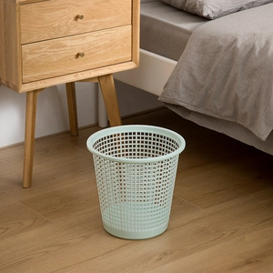 Light green hollow plastic waste basket with mesh design on a cozy bedroom wooden floor