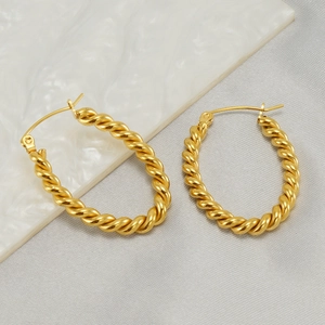 Fashionable 18k gold plated stainless steel twisted hoop earrings on marble background