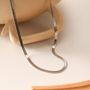 Elegant silver wide flat snake chain necklace made of stainless steel on ceramic decor