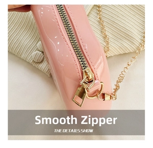 Detail of smooth gold metal zipper and chain strap on glossy pink jelly mini bag