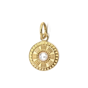 Close-up of a gold vintage steel pendant with a white pearl inlay and radial texture