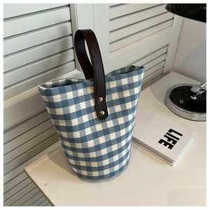 Blue and white checkered canvas bucket bag with brown leather handle on a desk