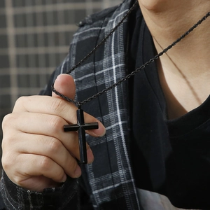Close-up of a minimalist black cross pendant with matching black rope chain in hand