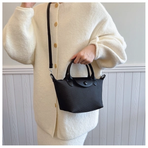 Detailed view of a black woven texture dumpling bag with leather handles and crossbody strap