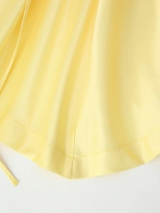 Detailed close-up of the smooth yellow satin fabric hem and thin strap on a mini dress