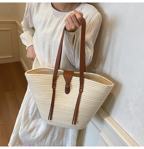 Detail of hand-held woven tote bag featuring beige straw texture and brown leather handles