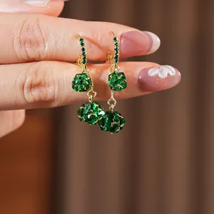 Vintage gold earrings with green crystal balls and pavé accents held by fingertips