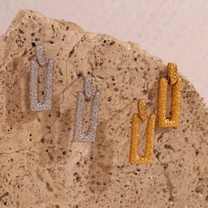 Macro shot of gold and silver rectangular earrings with lava texture on stone background