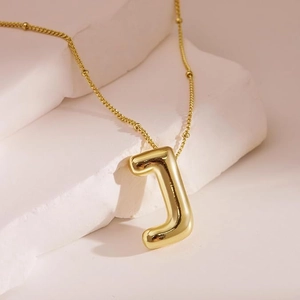 Close-up of golden letter J balloon pendant with a beaded chain on a textured surface