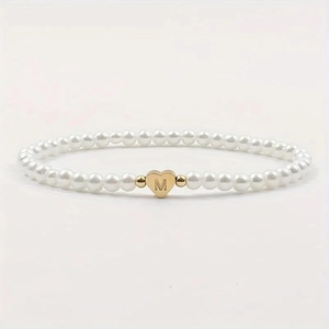 Macro shot of white pearls bracelet with a golden heart-shaped pendant engraved with M