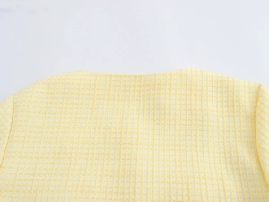 Close-up of the round neckline and yellow tweed textured fabric on the cropped jacket