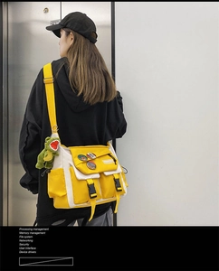 Detailed back view of a yellow canvas messenger bag with a green dinosaur charm pendant
