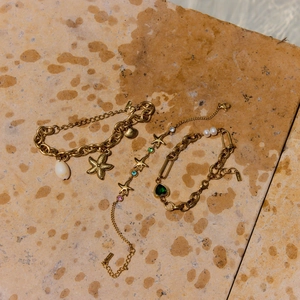 Close-up of golden starfish bracelets set with green heart gems and pearls on a stone base