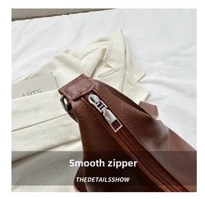 Detail shot of smooth silver zipper closure on brown leather tote bag with grainy texture