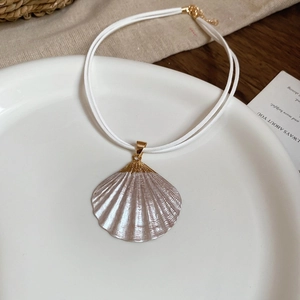 Flat lay of a pearl shell pendant necklace with white rope chain on a ceramic dish