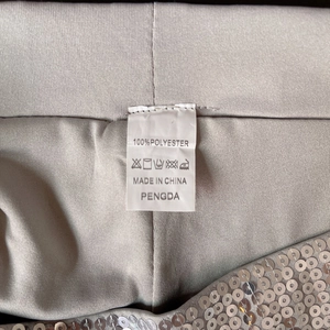Detailansicht des Pflegeetiketts aus 100% Polyester auf silbernen Pailletten-Shorts