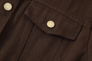Makrodetail von dunkelbraunem Denim mit Bronzeknöpfen und Naht der Pattentasche