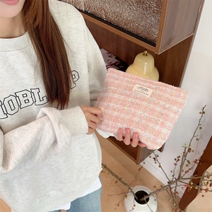 Detailed texture of pink tweed cosmetic bag with zipper and logo patch held by a hand