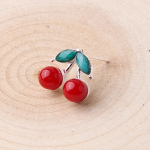 Detailed close-up of cute 3D cherry earring with red beads and green leaf on wood background