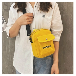 Yellow canvas crossbody bag with adjustable black strap worn by a model in casual outfit