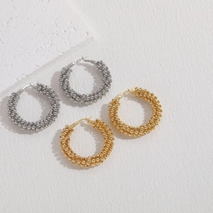 Close-up of gold and silver beaded texture hoop earrings on a minimalist stone base