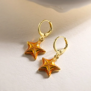 Close-up of gold-plated starfish earrings with orange enamel on a neutral surface