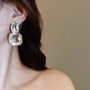 Close-up of a model wearing large rectangular crystal drop earrings with square cut diamonds