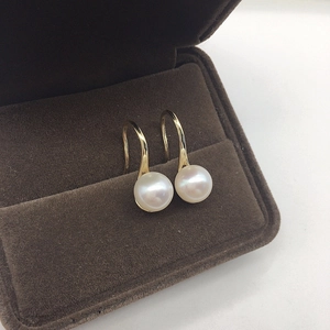 Close-up of lustrous freshwater pearl earrings with gold hooks in a brown velvet jewelry box