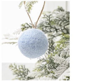 Close-up of a light blue wool felt ball ornament with jute rope on a snowy branch