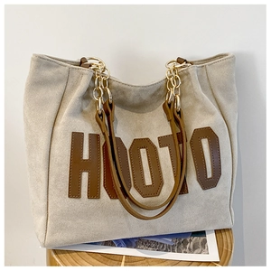 Detail of HOOTO large tote bag in beige with brown trim on a wooden stool