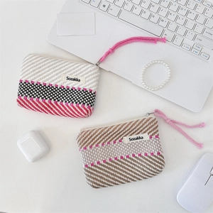 Detailed view of woven striped cosmetic pouches with zippers and lanyards on a desk