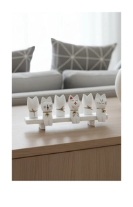 Detailed close-up of six white minimalist cat figurines with bells on a wooden stand