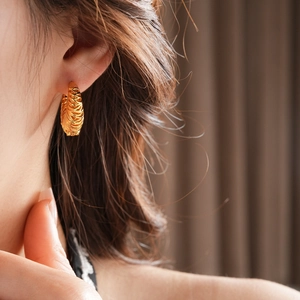 Detailed view of an 18k gold plated hoop earring with intricate feather leaf textures on ear