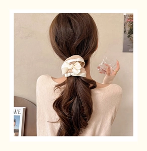 Detail of elegant beige satin bow hair tie on a bun showing texture and glossy finish