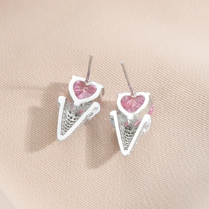 Macro shot of silver ice cream earrings with pink heart zircon stones on beige fabric