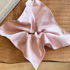 Detail of light pink satin scrunchie showing fabric sheen and pleated texture on wood