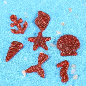 Macro detail of red resin anchor and starfish ornaments on blue sand background