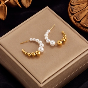 Detail shot of C-shaped drop earrings with white pearls and gold metal beads on velvet